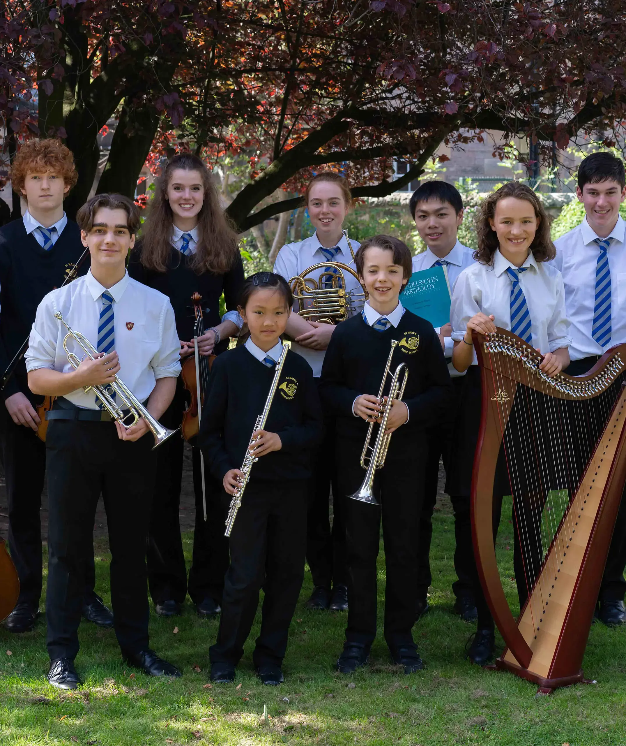 St. Mary's Music School pupils standing outside under a tree with their instruments